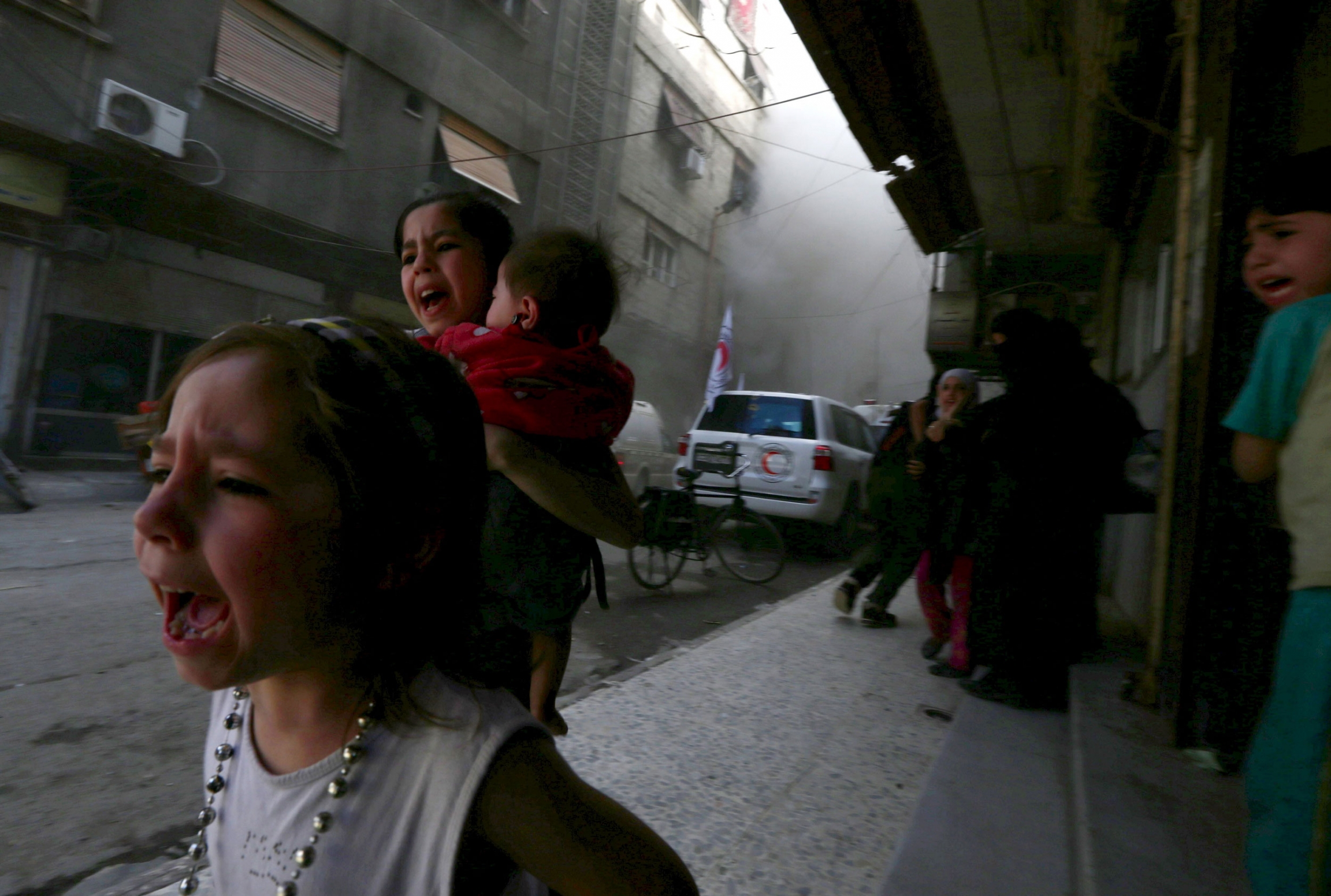 Ghazal, 4, (left) and Judy, 7, carrying 8-month-old Suhair, run away after the shelling of a Red Crescent convoy in Damascus, Syria, May 6, 2015. Ghazal, 4, (left) and Judy, 7, carrying 8-month-old Suhair, run away after the shelling of a Red Crescent convoy in Damascus, Syria, May 6, 2015.