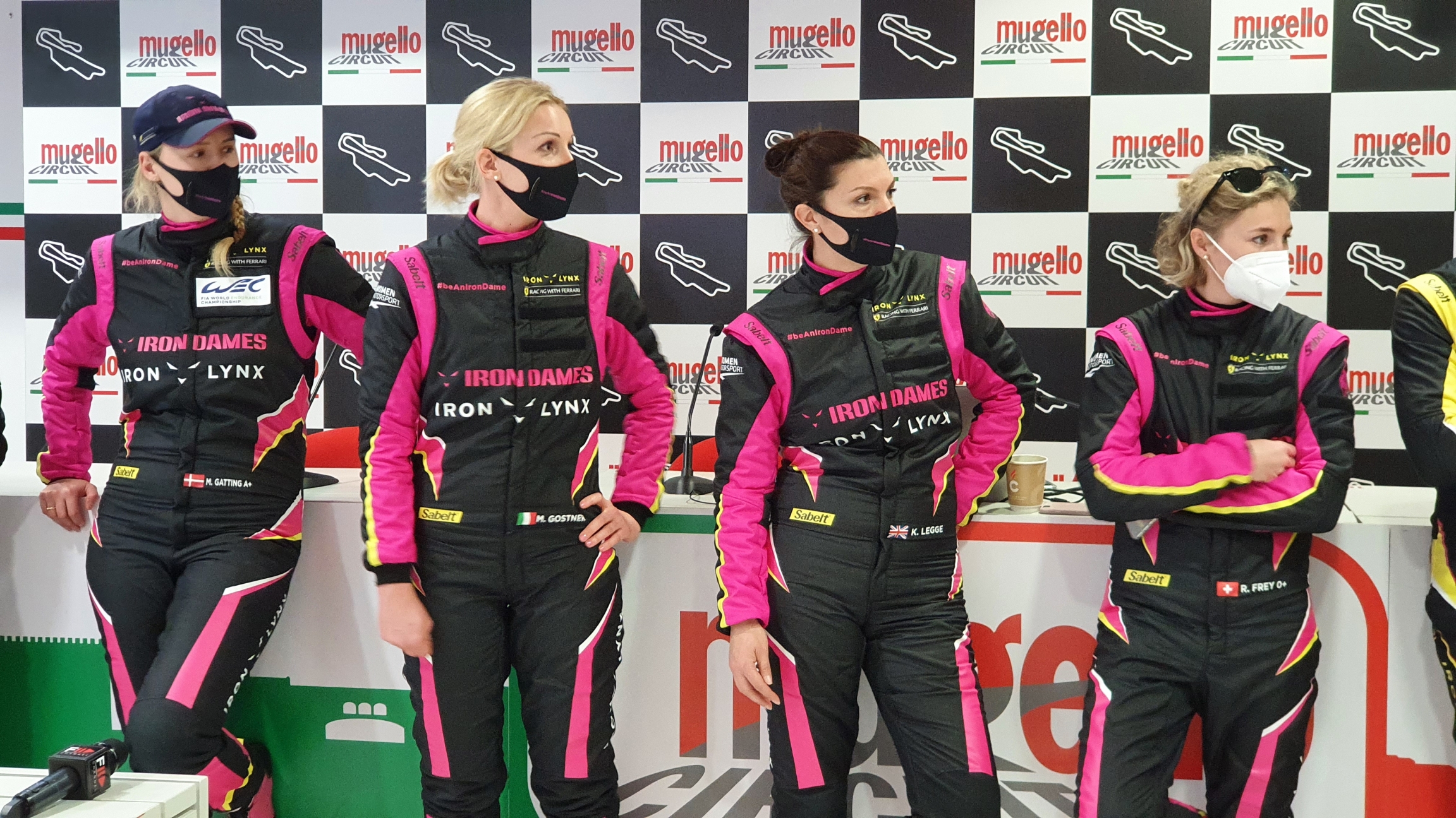 Iron Dames pose for a portrait at Mugello. Four women wear black and pink race tracksuits.