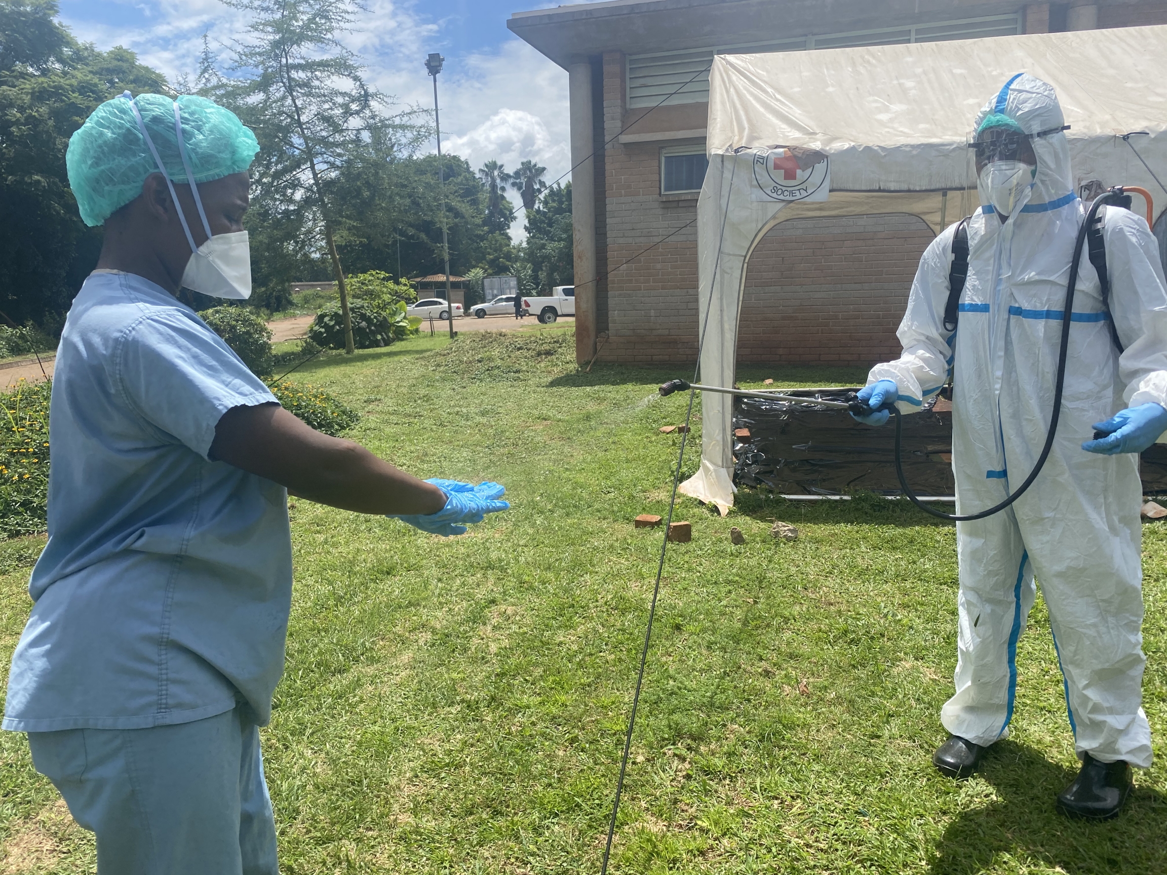 A health official disinfects a colleague at the Zimbabwean's main vaccination center at Wilkins Hospital, March 31, 2021, in Harare, Zimbabwe. A health official disinfects a colleague, both wear protective gear.