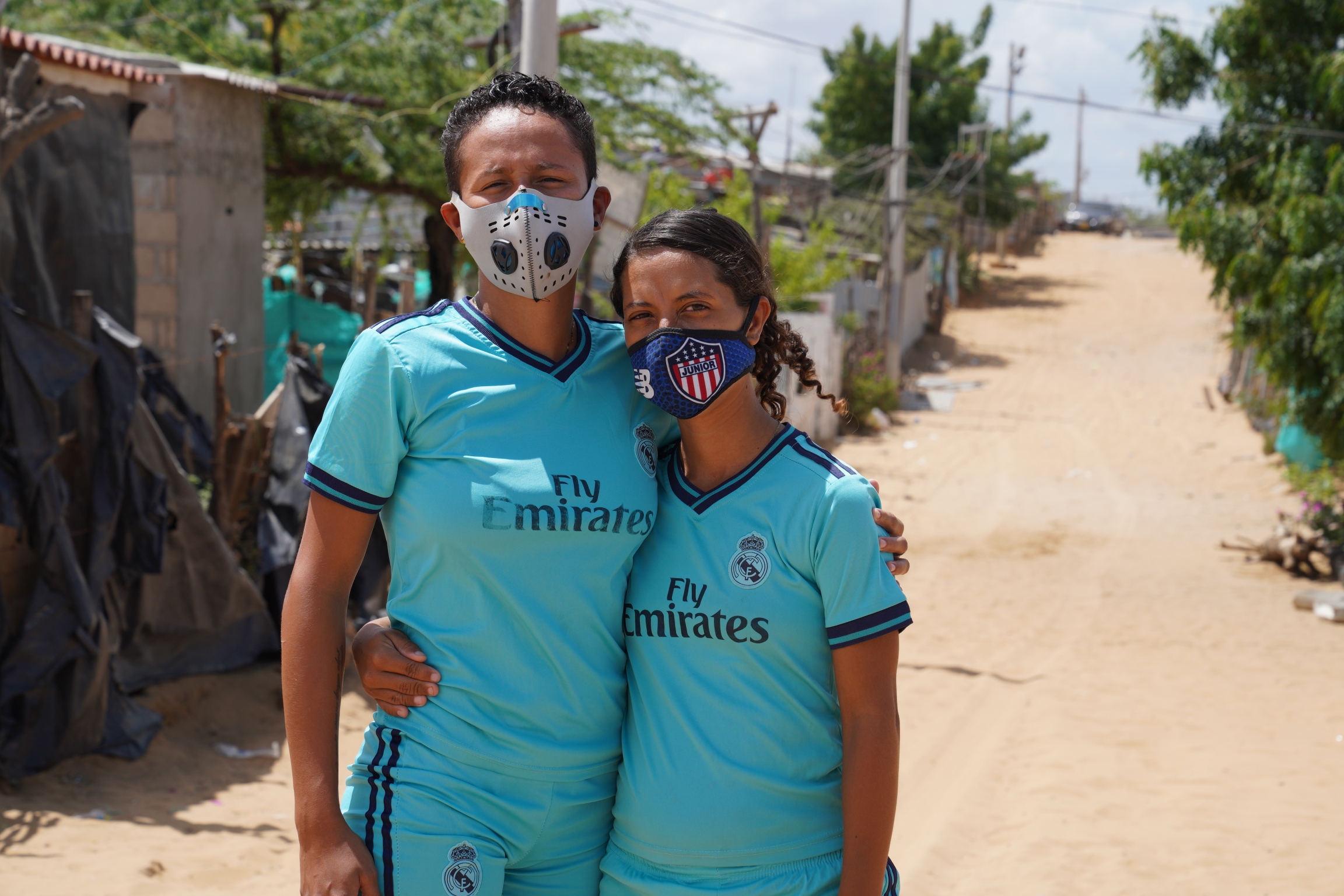 Team captain Gibel Gonzalez (right) says that in Venezuela she played kickball casually. Two kickball players wearing blue uniforms pose for a photo with their arms around each other