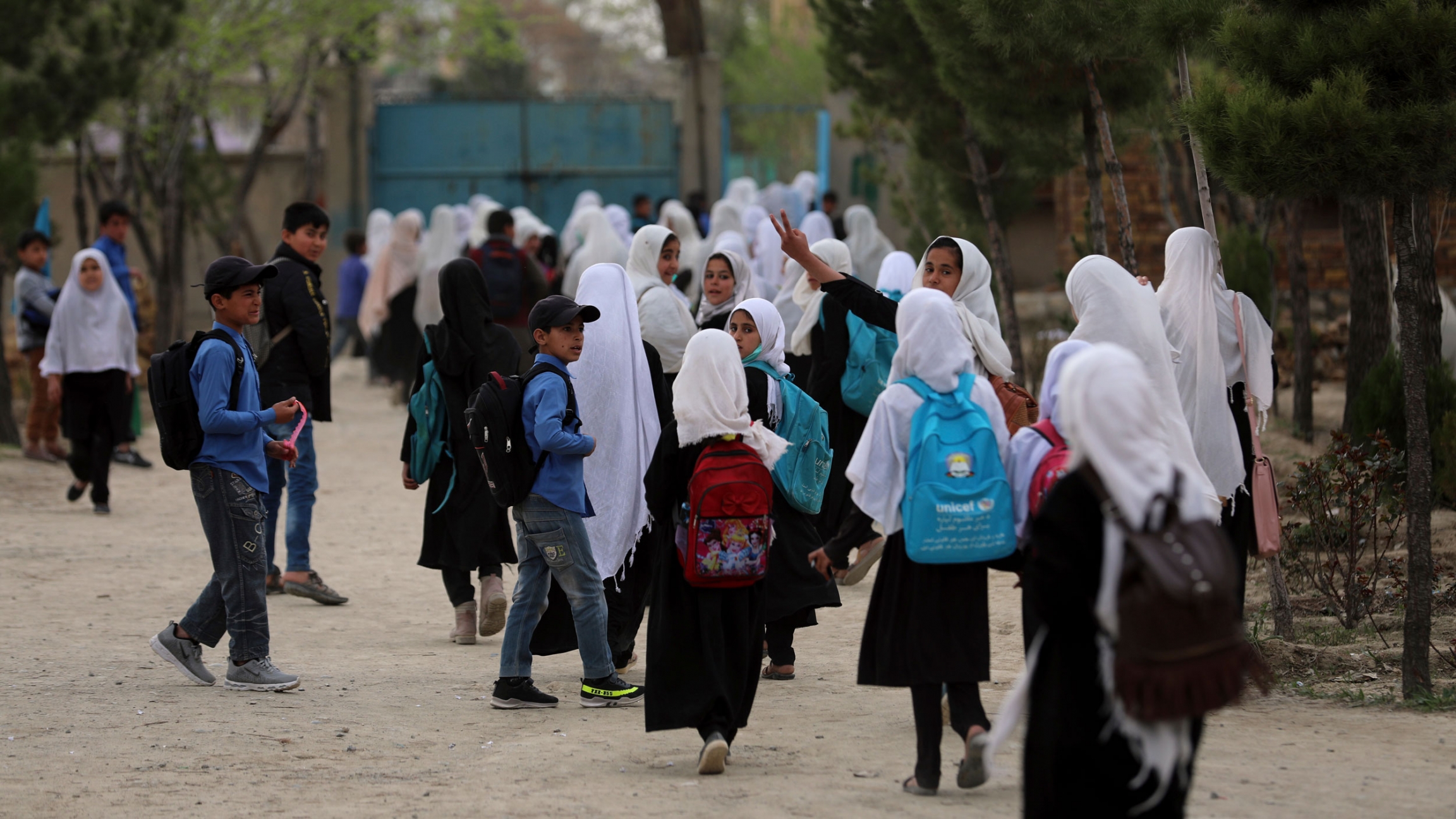 Afghan students leave school classes in a primary school in Kabul, Afghanistan, March 27, 2021. A crowd of young people are shown walking near a school with many girls wearing a white head covering.