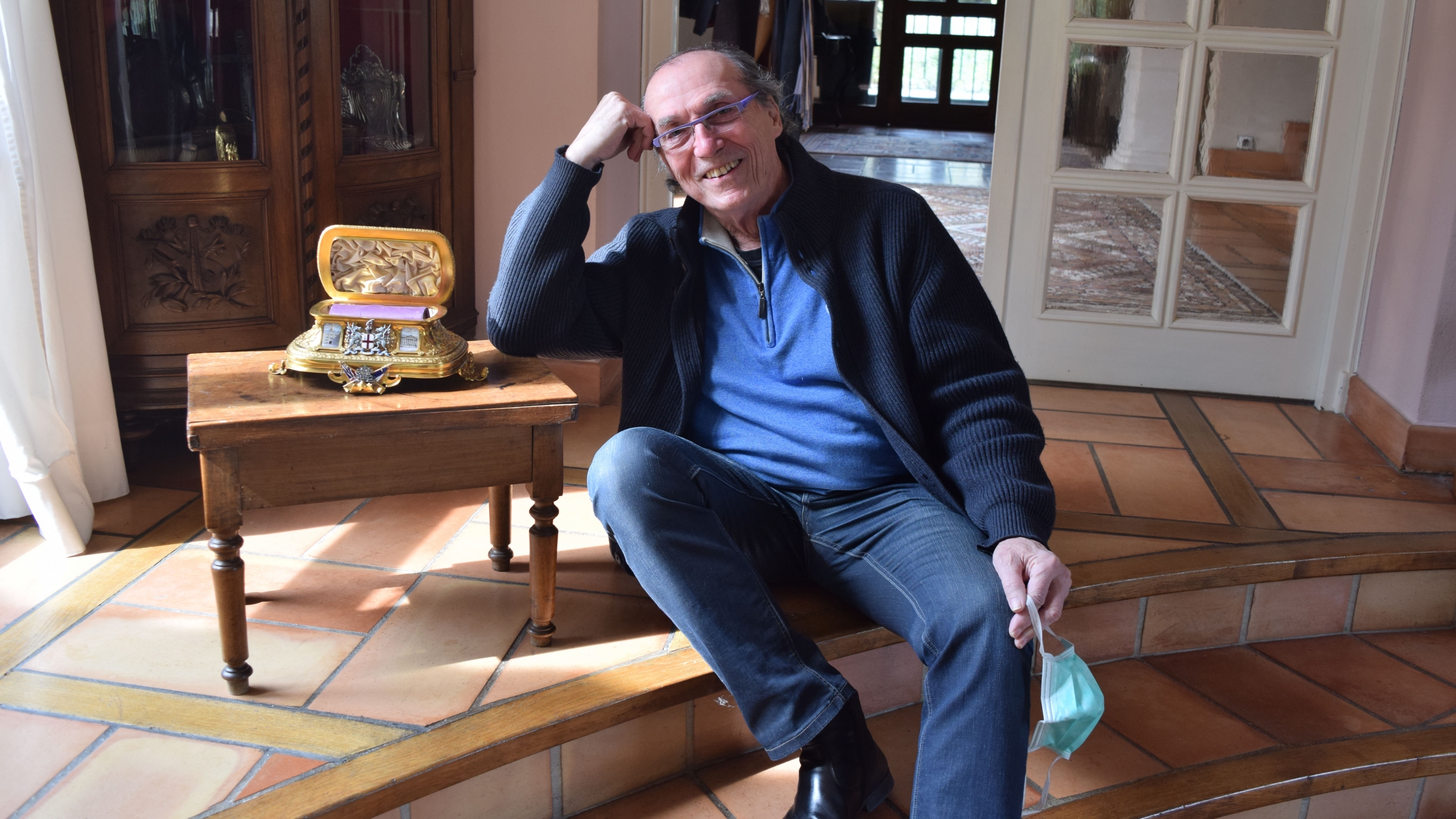 Michel Becker, an antique dealer, sits next to the golden casket featured in his treasure hunt, “The Golden Treasure of the Entente Cordiale." An older white male sits next to a tiny golden casket and smiles