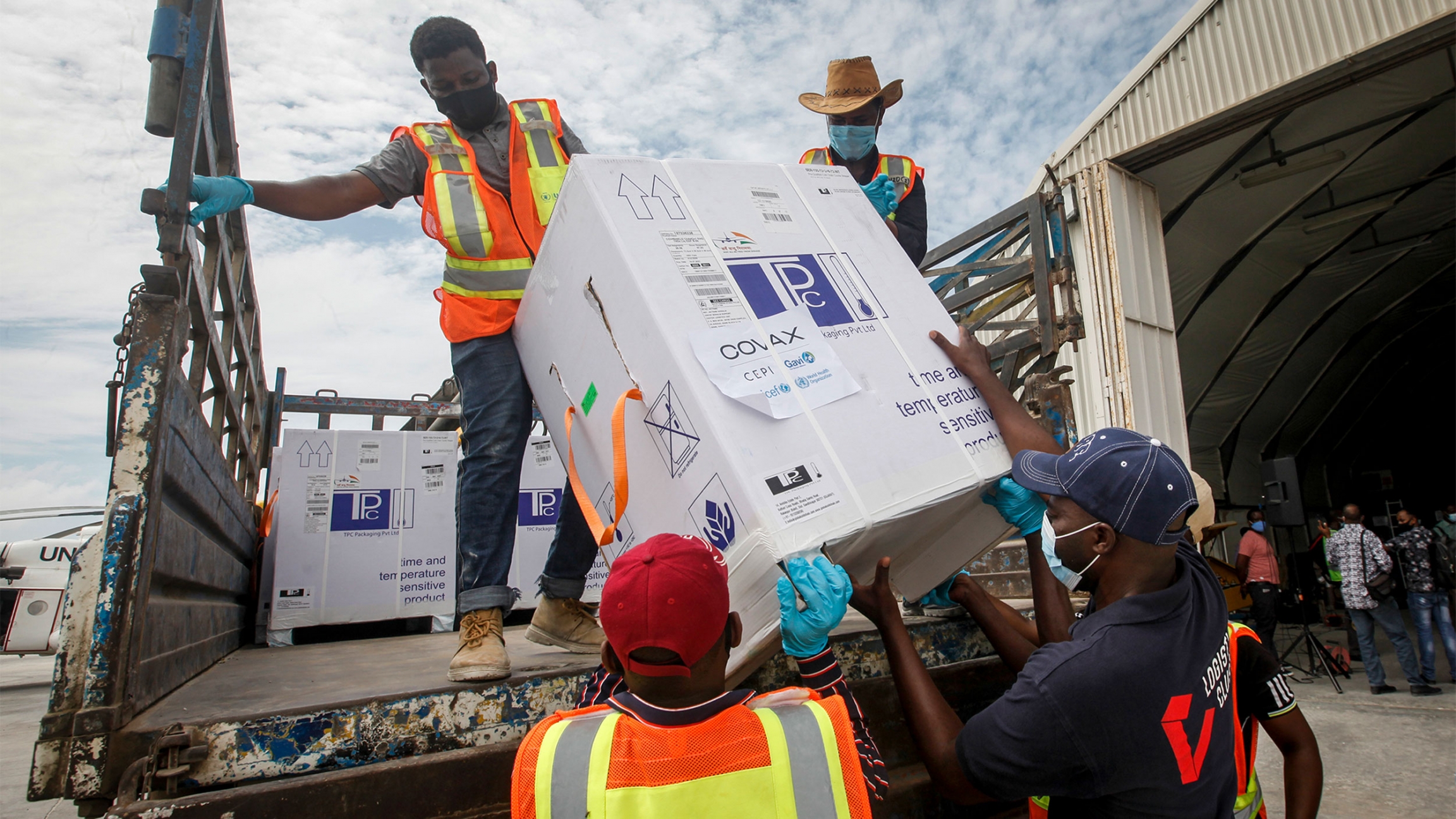 Vaccines from India arrive in Somalia through COVAX Men in orange and yellow jackets lift a box of vaccines from COVAX off of a truck bed