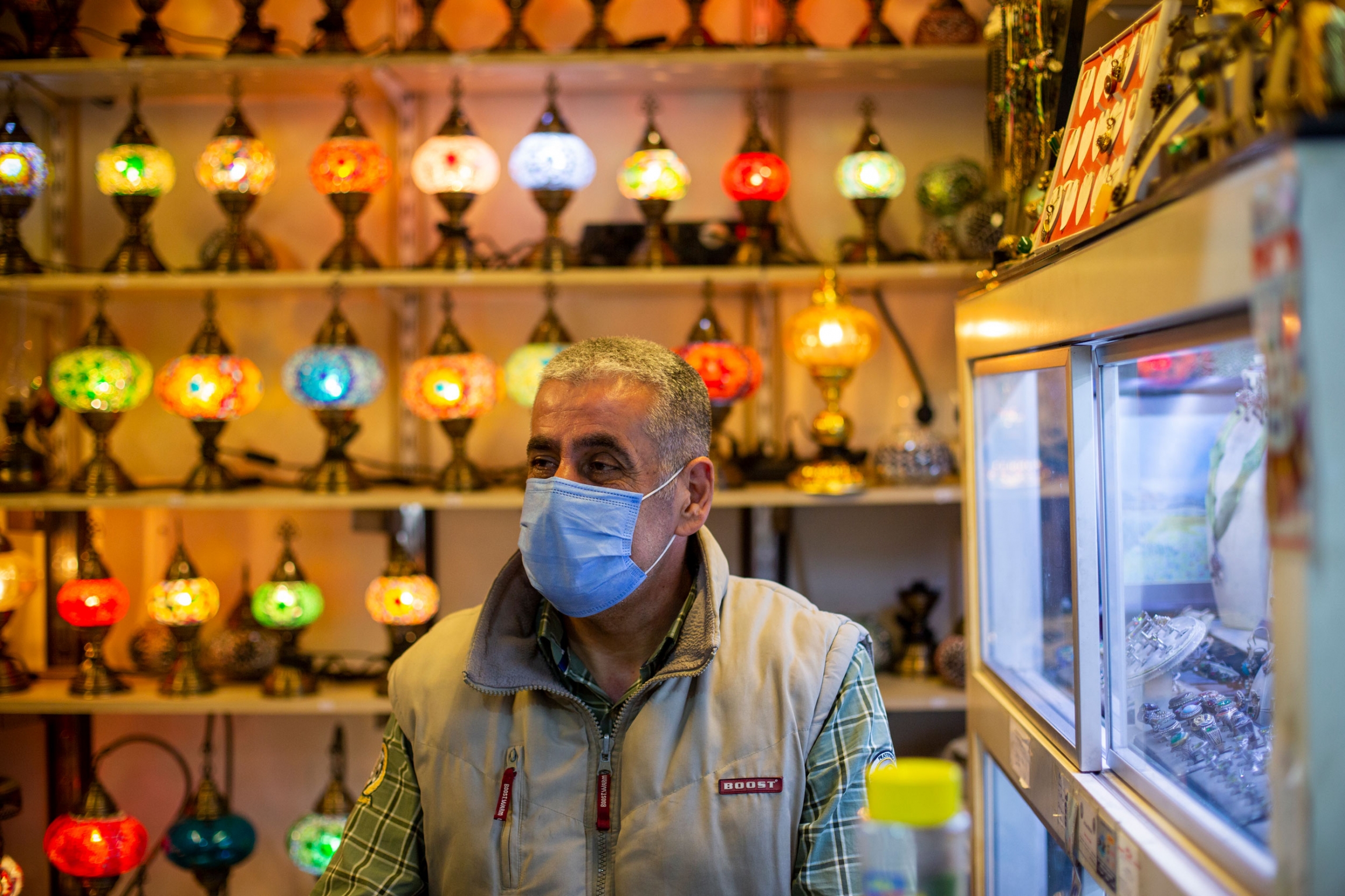 Kemal Kirdar at his souvenir shop in Istanbul. A man is shown with a face mask and standing in front of a wall of brightly colored lamps.