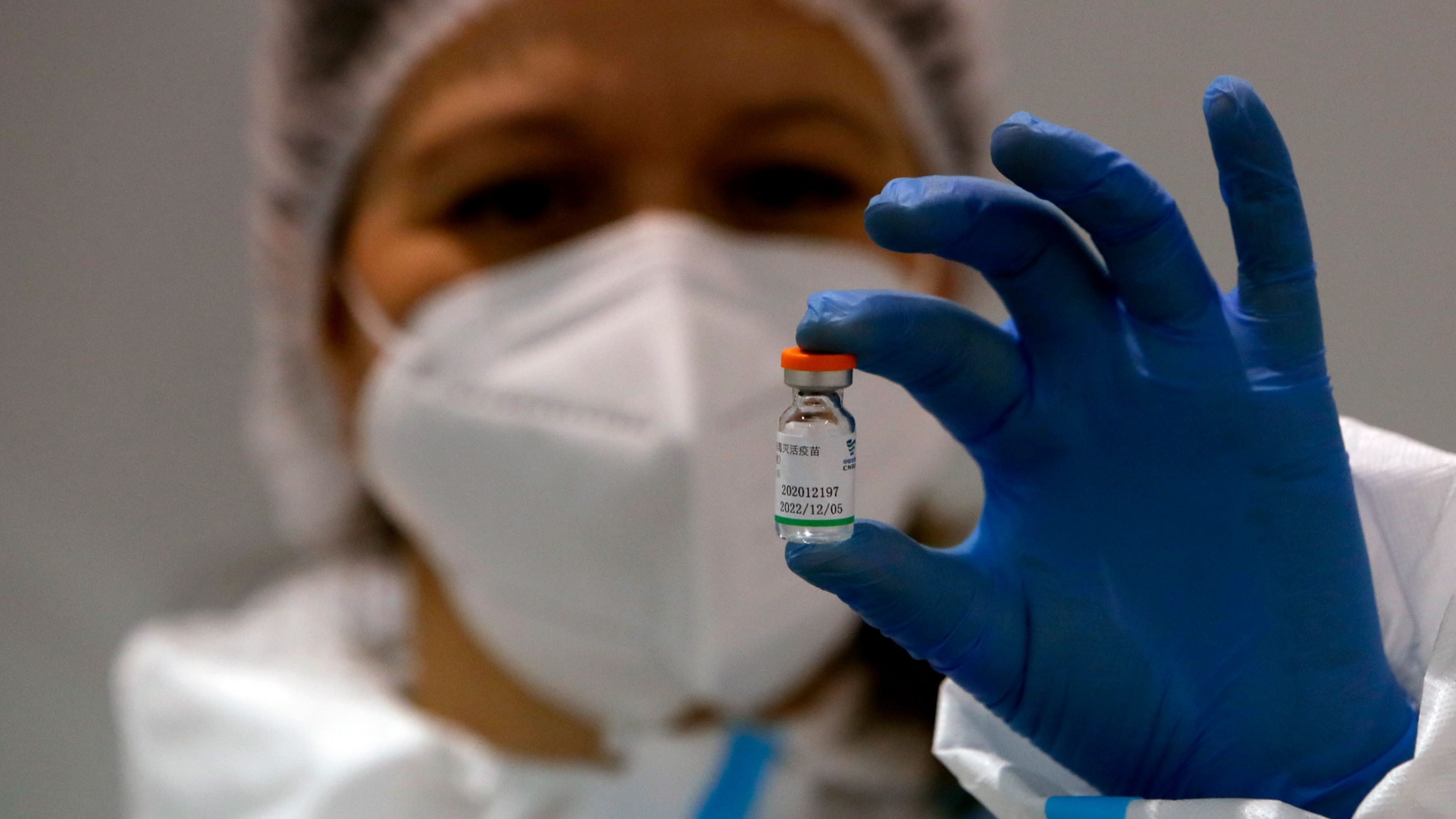 A medical worker poses with a vial of the Sinopharm's COVID-19 vaccine in Belgrade, Serbia, Jan. 19, 2021. A person is shown wearing a protective medical mask and hair net while holding between their finfers a file of the Sinopharm's COVID-19 vaccine.
