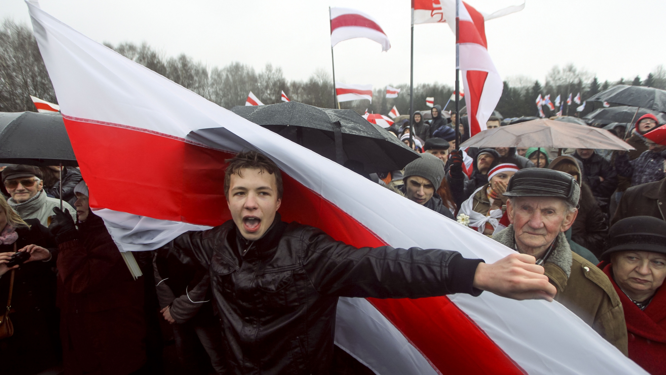 A prominent opponent of Belarus' authoritarian president, Roman Pratasevich, attends an opposition rally in Minsk, Belarus in 2012. Man in black jacket holding red and white flag
