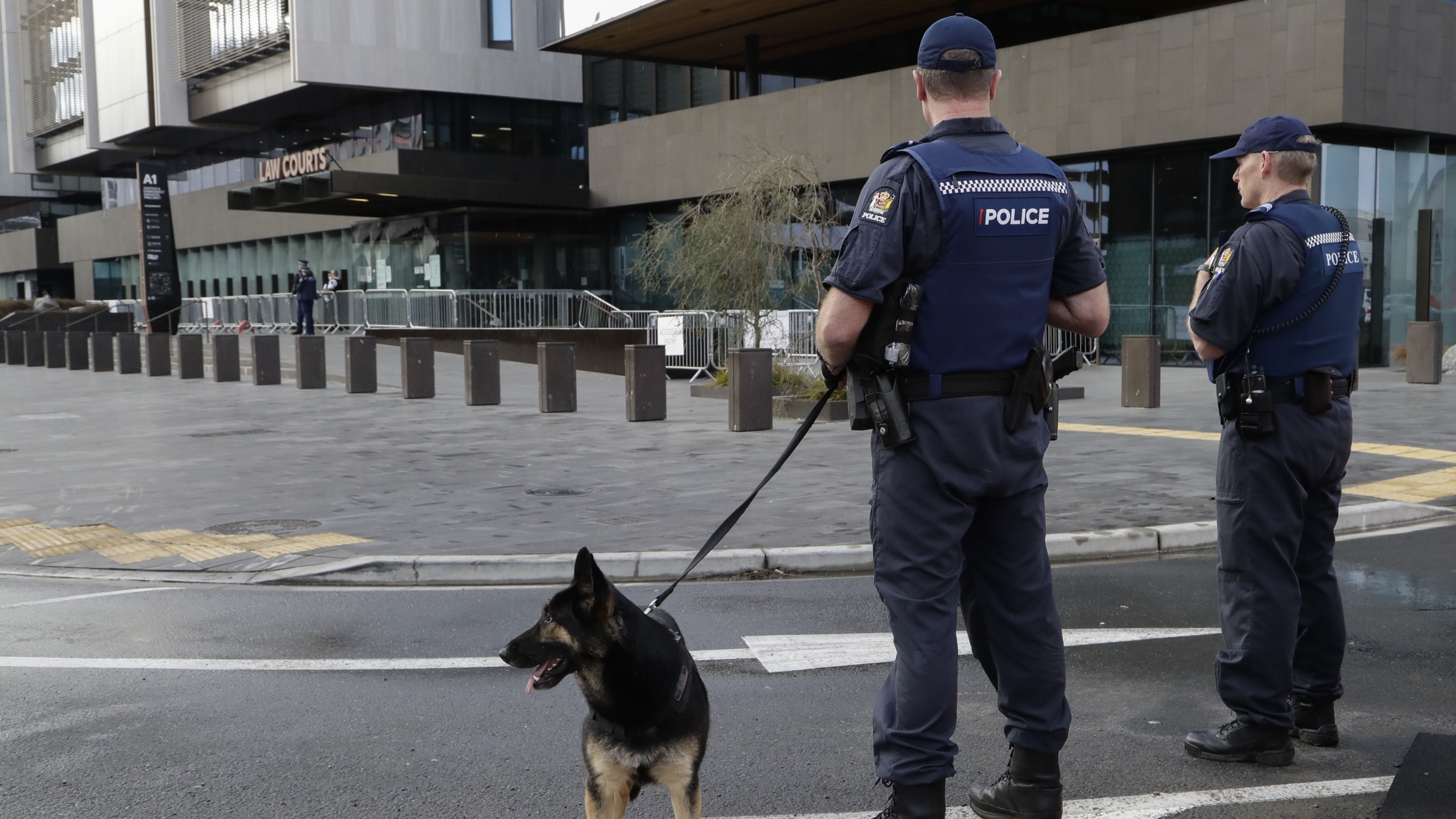 Police keep watch outside the Christchurch High Court ahead of day two of the sentencing hearing of Australian Brenton Harrison Tarrant, in Christchurch, New Zealand. Armed police stand in front of a building with a police dog