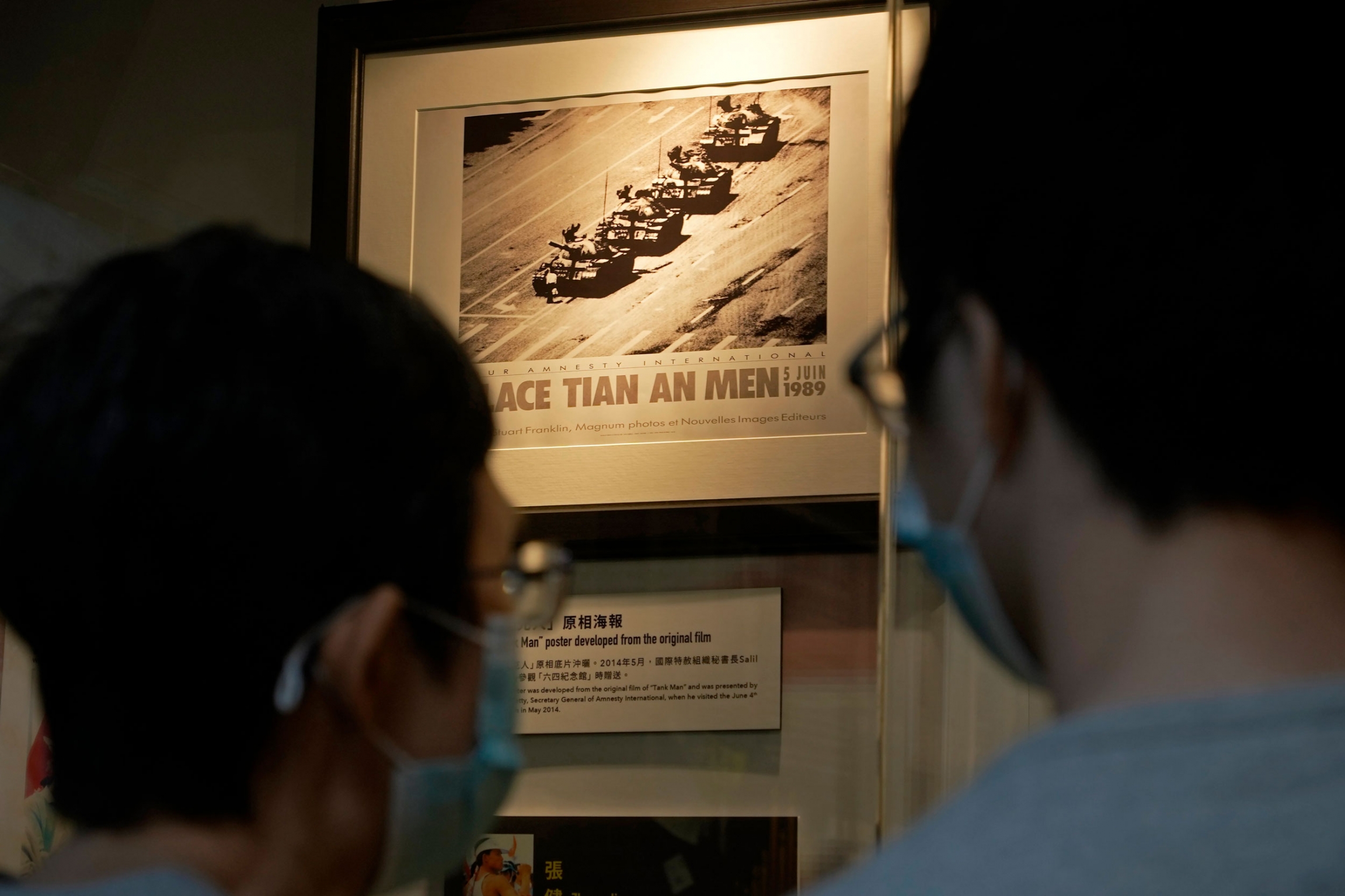 A picture showing a man blocking a line of tanks at the 1989 pro-democracy movement in Beijing is displayed at the "June 4 Memorial Museum." Two people are shown wearing protective face masks and looking at a photograph of a man blocking a row of four tanks.