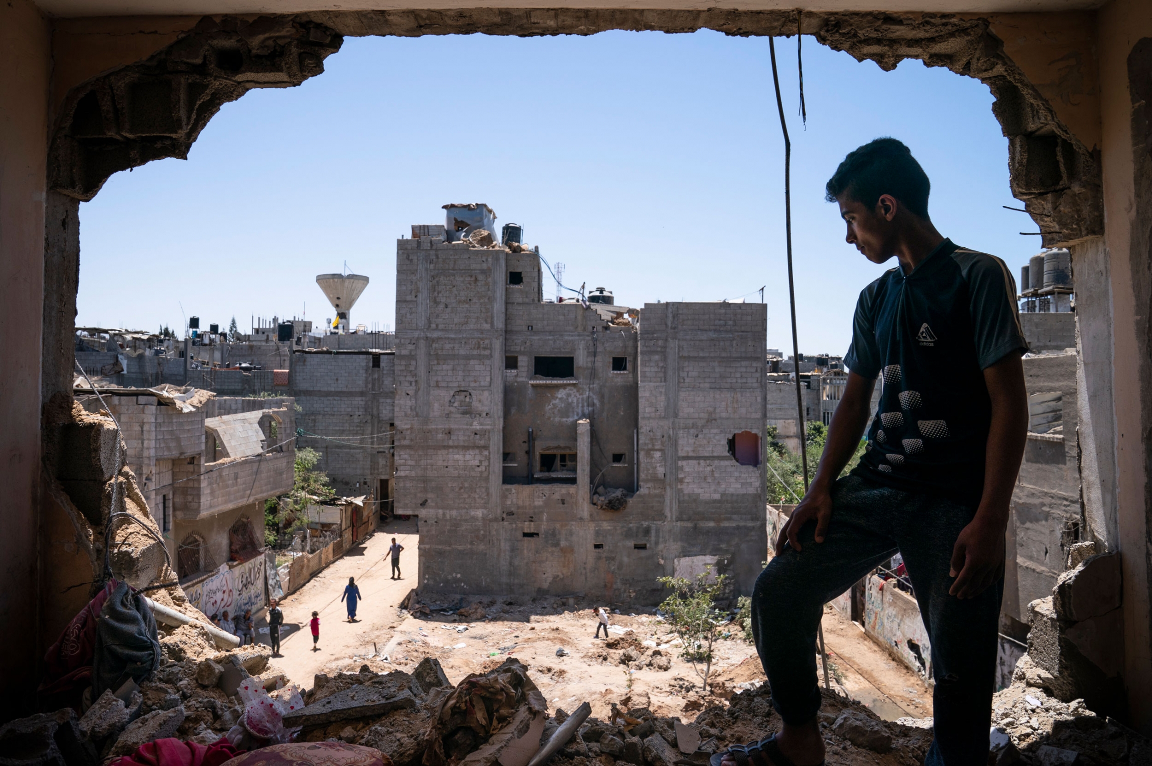 Mahmoud Al-Masri, 14, stands for a portrait in his damaged bedroom in Beit Hanoun, Gaza Strip, May 26, 2021. A young person stands in the bombed hole where a wall once stood.