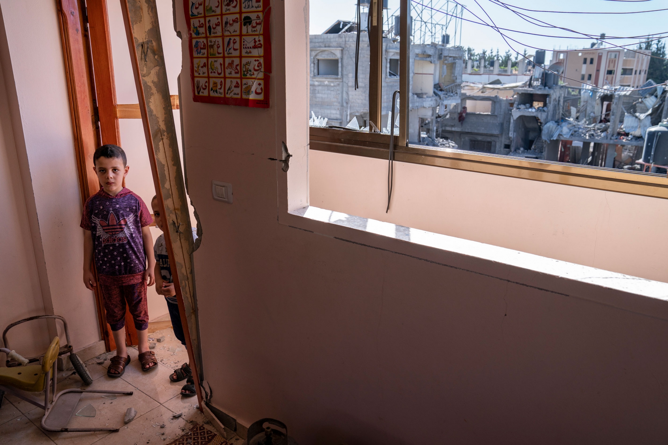 Awny Abed, 6, left, and his brother Salem, 5, stand for a portrait in their damaged bedroom, in Maghazi, Gaza Strip, May 27, 2021. Two young boys are shown standing in a damaged door frame.