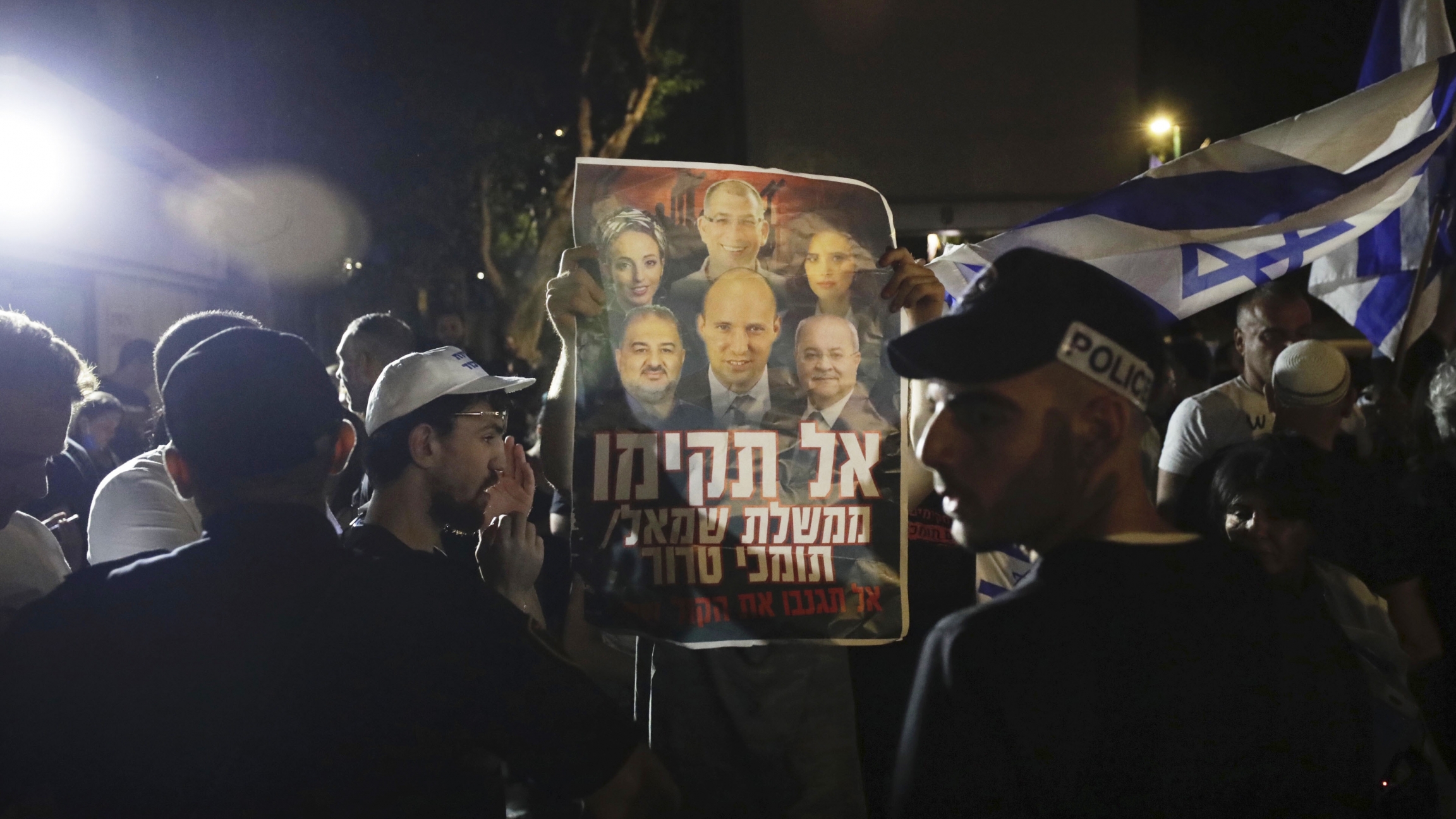 Israeli police officers stand guard as right-wing protesters chant slogans and hold signs showing Naftali Bennett, and other members of the Yamina party, with Arab politicians Ahmad Tibi, right, and Mansour Abbas, left, during a demonstration. Israeli police officers stand guard as right-wing protesters chant slogans and hold signs.