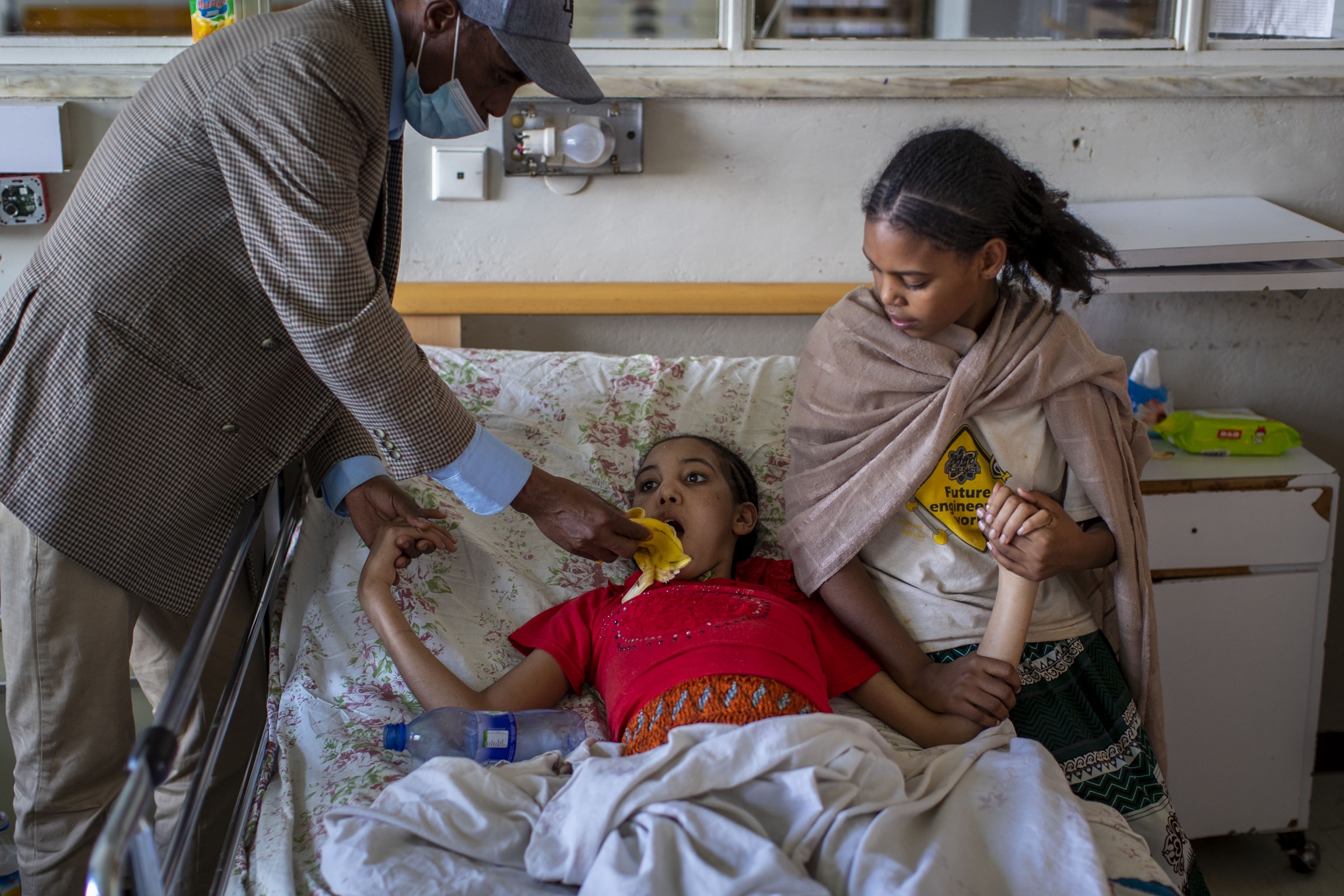 Akhberet Tadesa, 15, who is unable to feed herself and hasn't spoken or walked unaided since a shell exploding near her home left her in an apparent state of mental shock, is aided by her father Tadese Gebremedhin, left, and sister Fana, 13, right. A girl in red rests on bed with her father and sister helping her.