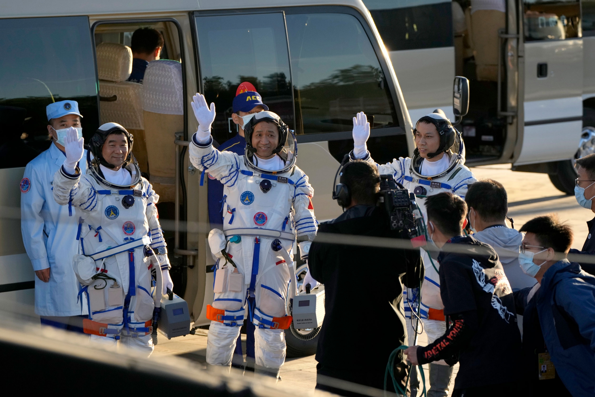 Chinese astronauts, from left, Liu Boming, Nie Haisheng, and Tang Hongbo wave as they prepare to board for liftoff at the Jiuquan Satellite Launch Center. Chinese astronauts are shown wearing white and blue stripped space suits and waiving.