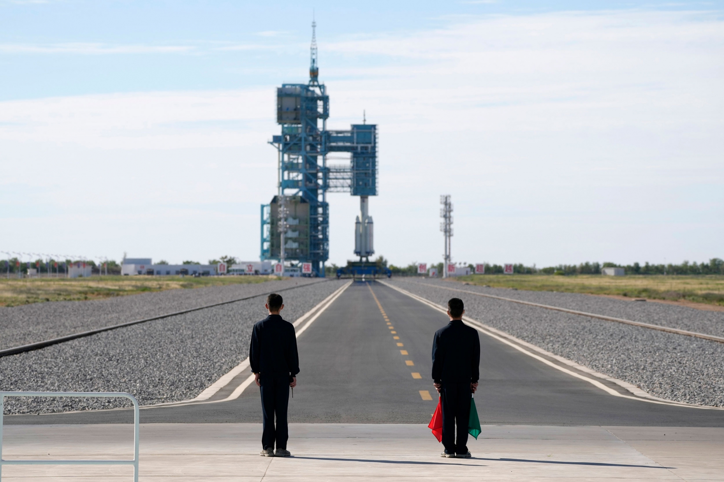 Officials stand on the tarmac ahead of the liftoff at the Jiuquan Satellite Launch Center in Jiuquan in northwestern China, Thursday, June 17, 2021. Two people are shown at the end of a long tarmac with the Chinese spaceship set for launch in the distance.