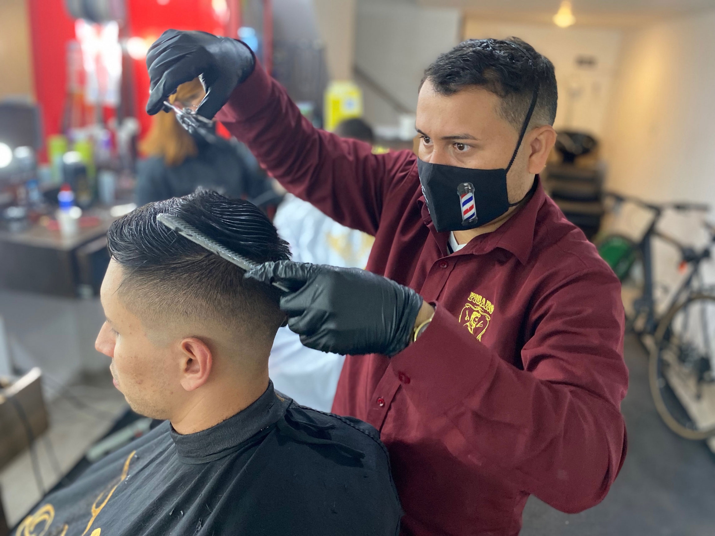 Dennis Revilla, 36, is still ineligible to get a coronavirus vaccine from the government. He works at a small barbershop that is not part of the privately funded vaccination drive. A man cuts another man's hair at a barber shop.