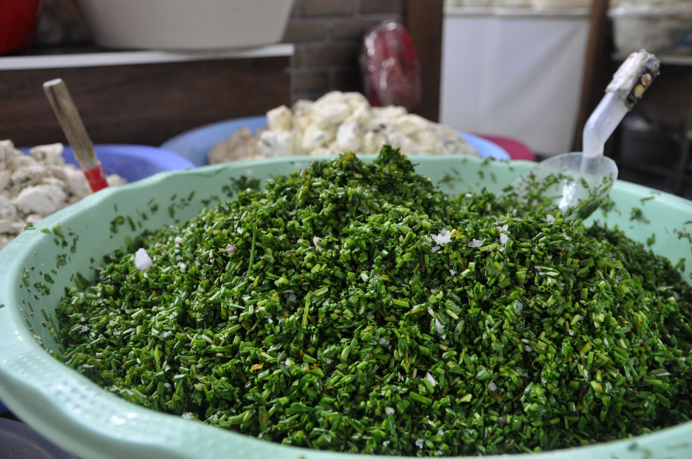 Herbs used in Van Otlu Peyniri vary, but are generally collected in the mountains by village children after the snowmelt. They include wild garlic or leeks, mountain thyme, fennel, or mint, and wildflowers. Green herbs used in Van Otlu Peyniri mixed in a green bowl.
