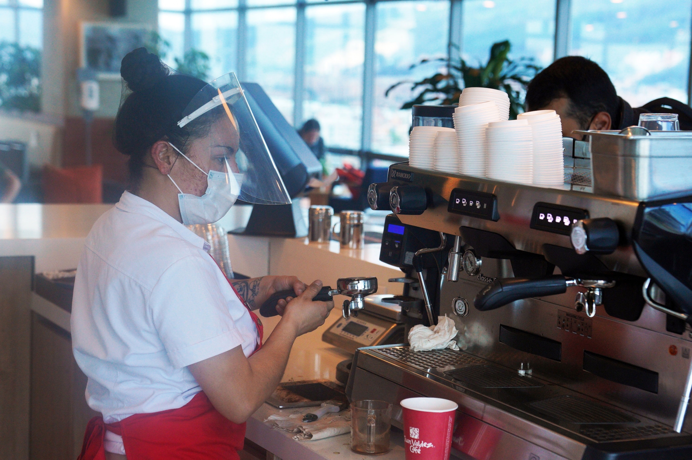 As a barista for the Juan Valdez coffee chain, Sandra Salazar is often in contact with customers. So the 28-year-old was relieved when her company announced it had purchased vaccines for its employees. Sandra Salazar wears protective gear as a barista behind the counter.