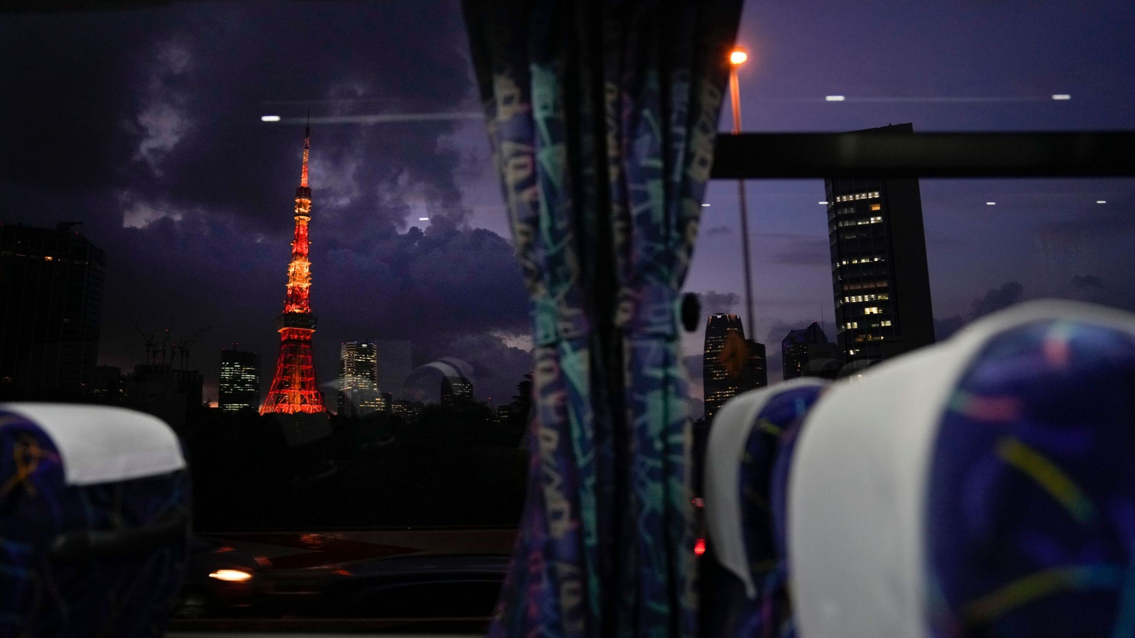 The Tokyo Tower is seen through a bus window ahead of the delayed 2020 Summer Olympics on July 15, 2021. The Tokyo Tower is shown in the distance illuminated with red and orange lighting.