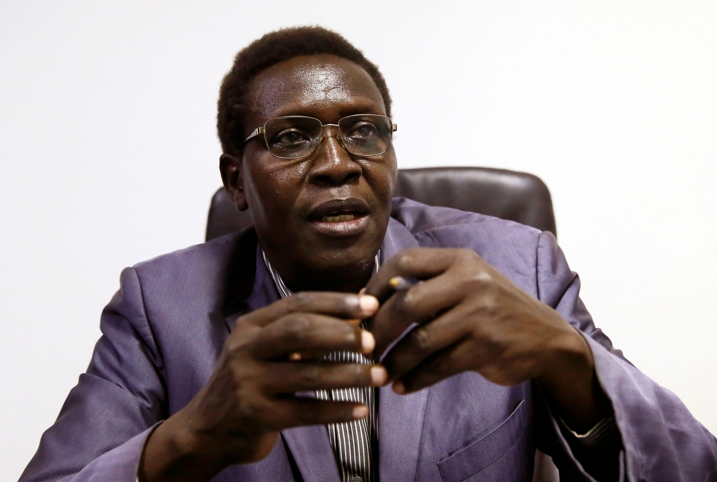 Guma Kunda Komey speaks during a meeting at his office. A man is shown wearing a purple suit jacket and wearing glasses.