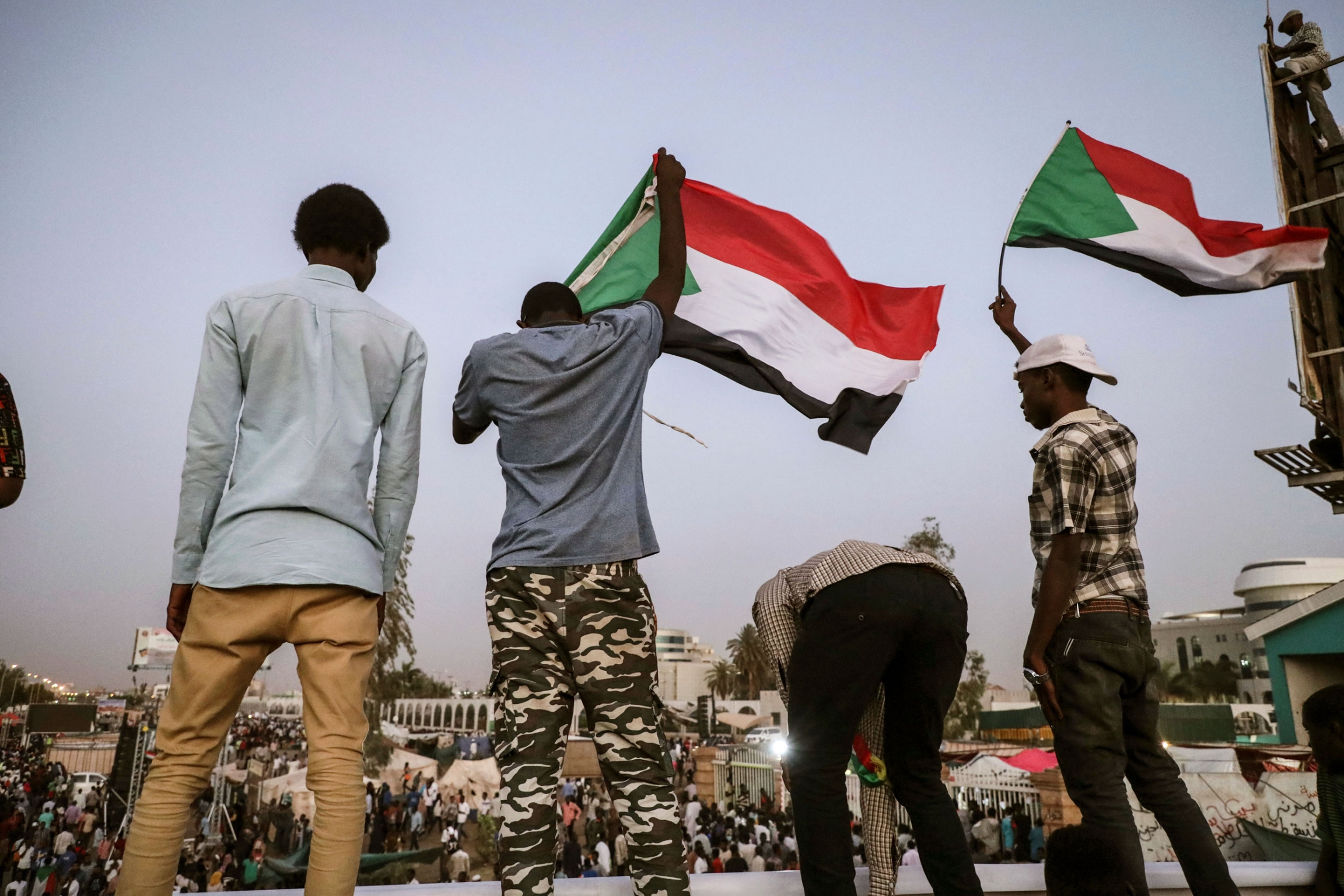 Sudanese protesters chant slogans during a rally outside the army headquarters in Sudan's capital Khartoum, April 20, 2019. A group of four men are shown with two waving the Sudanese national flag.