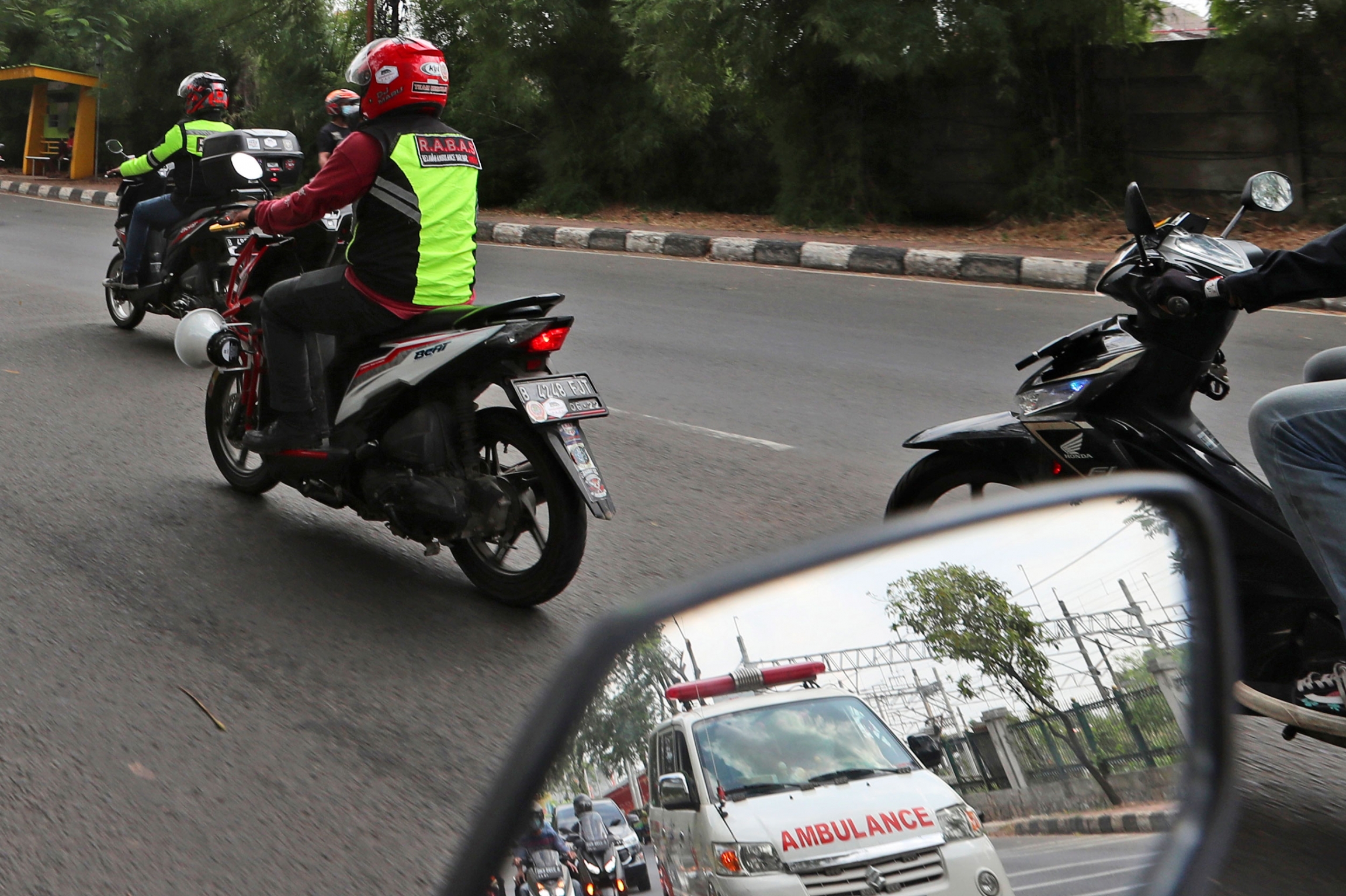 Motorcycle volunteers escort an ambulance on the outskirts of Jakarta, Indonesia. An ambulance is shown in the reflection of a motorbike's side view mirror.