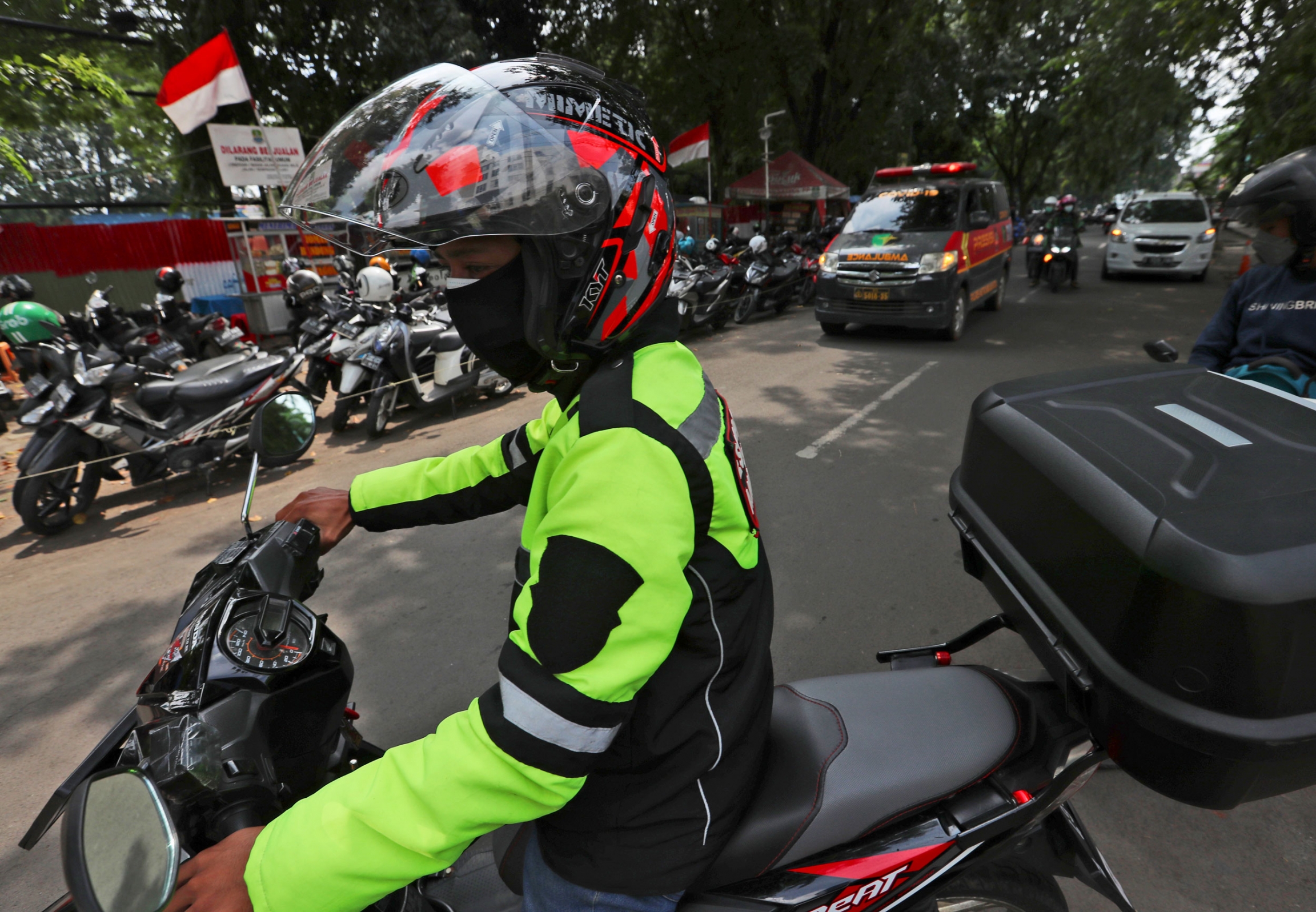 The two-wheeled volunteers like this provide a key service in the sprawling metropolis of Jakarta, Indonesia, where ambulances struggle to serve all those in need because of a surge in coronavirus infections. A close up photograph of a man wearing a reflective jacket and helmet while riding a motorbike.