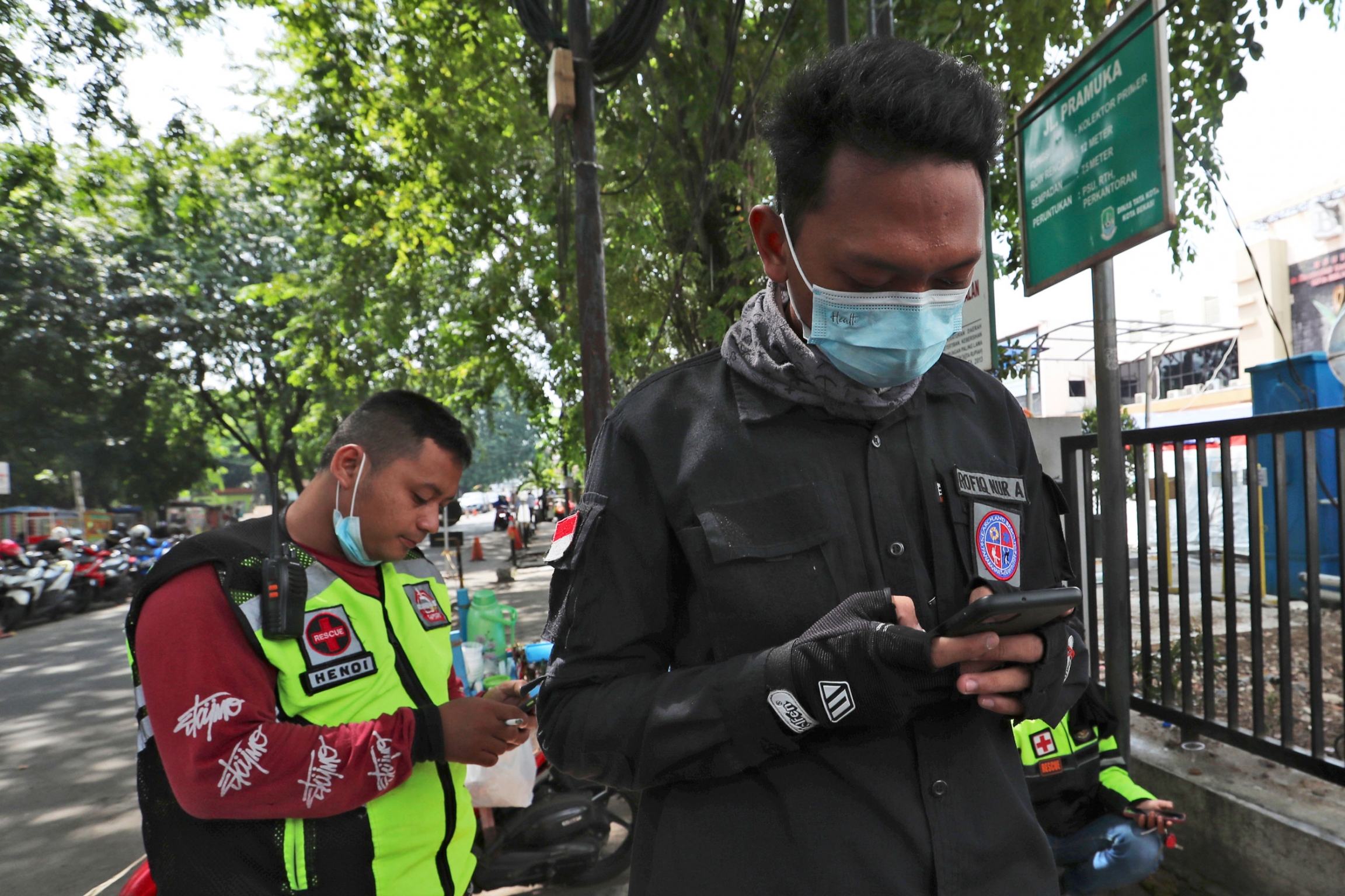 Motorcycle volunteers Hendi and Rofiq Nur check their mobile phone as they take a break in Bekasi on the outskirts of Jakarta, Indonesia. Two men are shown looking down at their mobile phones while wearing medical face masks.