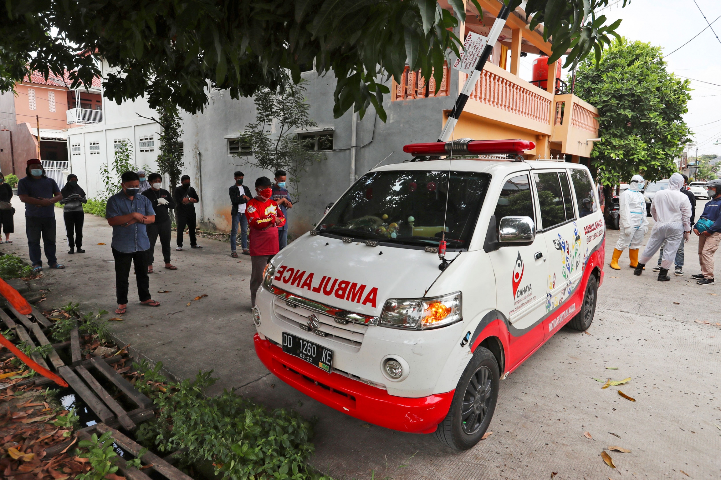 Volunteers join relatives to pray near an ambulance carrying the body of a COVID-19 victim prior to escorting it to a cemetery for burial, in Bekasi on the outskirts of Jakarta, Indonesia. Several people are shown socially distanced near a white and red ambulance.