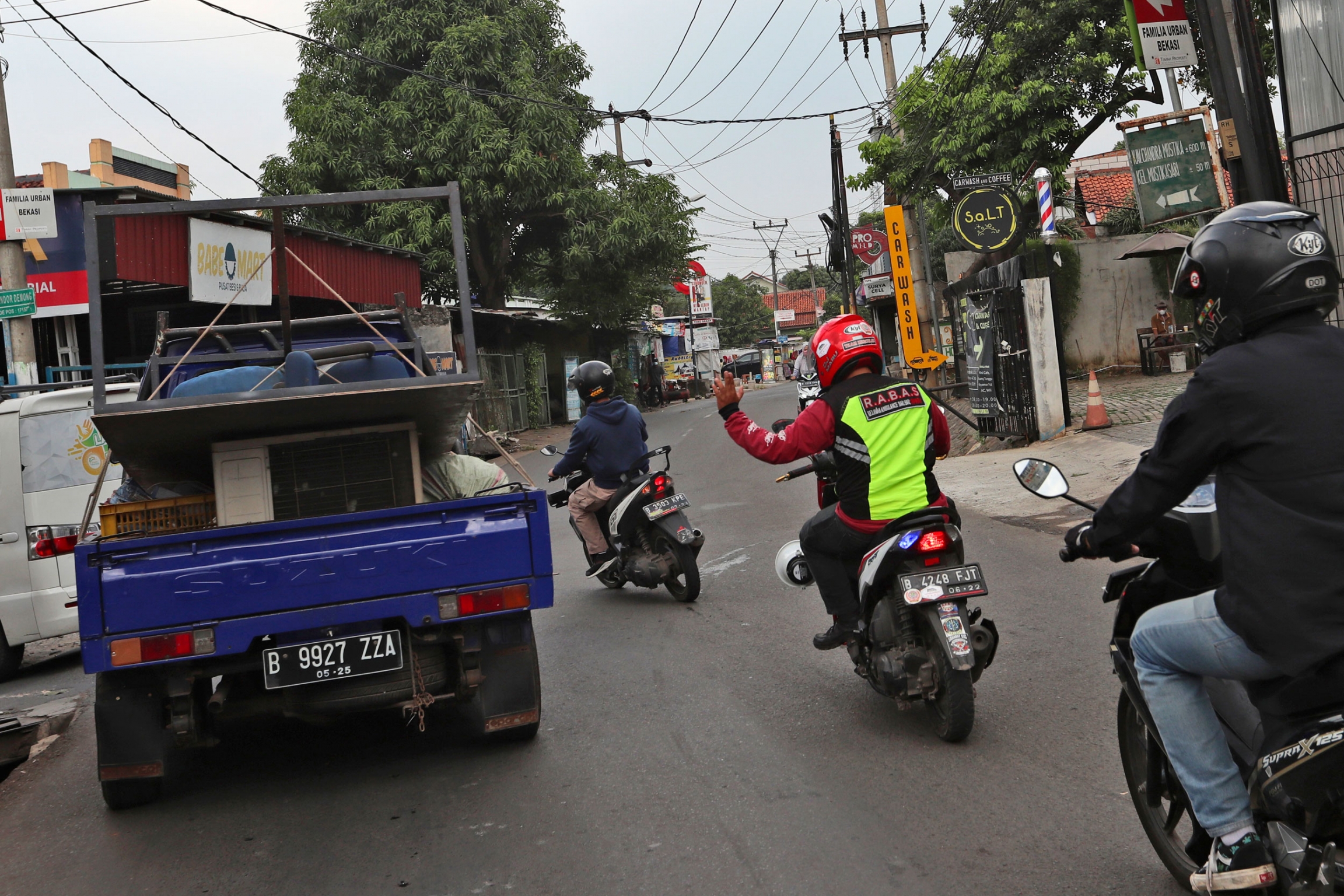 Motorcycle volunteers clear traffic for an ambulance carrying the body of a COVID-19 victim. Three people on motorbikes are shown with one holding his hand up to a truck to clear the road for an ambulance.