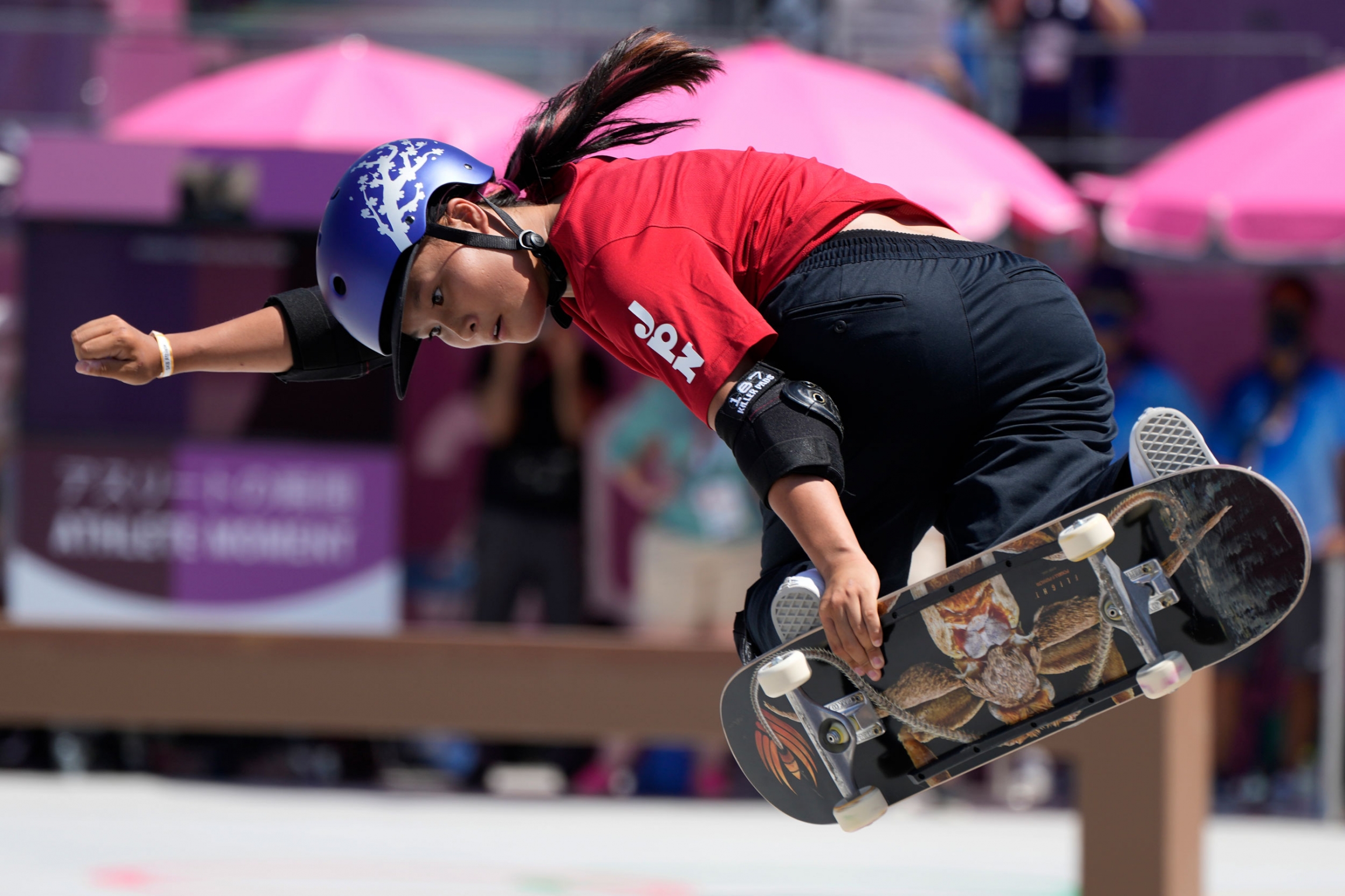 Sakura Yosozumi performs a trick in the women's park skateboarding finals at the Tokyo Olympics, Aug. 4, 2021. Sakura Yosozumi is shown in mid-air holding her skateboard to her feet.