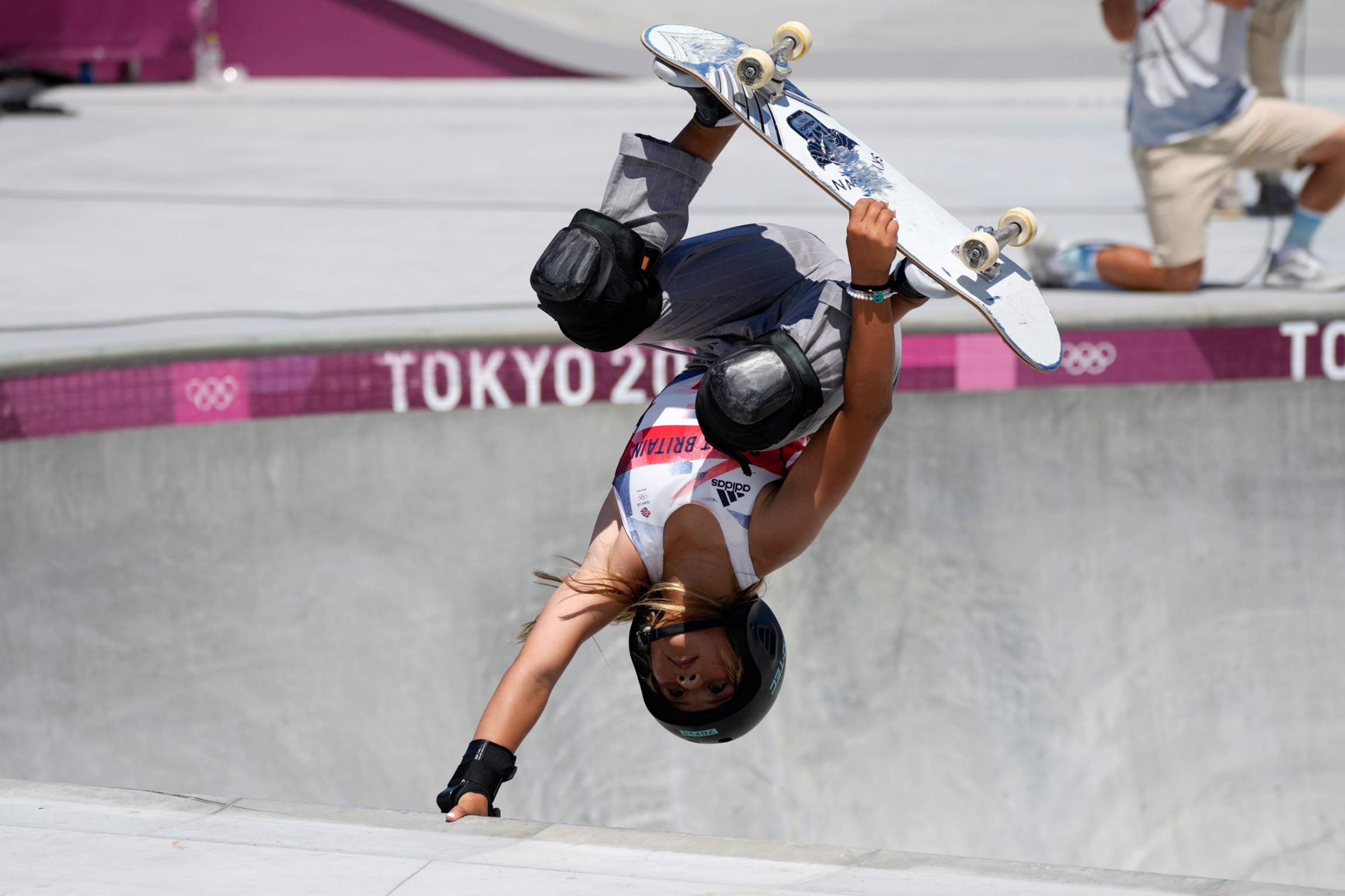 Sky Brown of Britain competes in the women's park skateboarding finals at the 2020 Summer Olympics, Aug. 4, 2021. Sky Brown of Britain is shown upside down with her skateboard held against her feet and her right arm holding on to the edge of the park bowl.