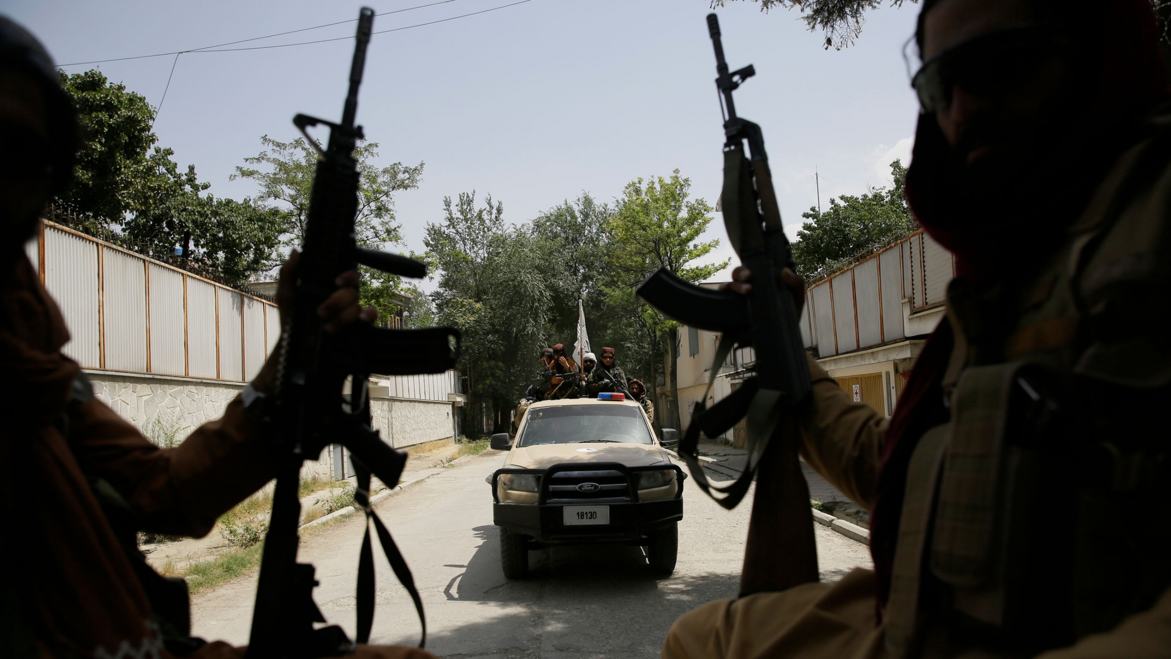 Taliban fighters patrol in Kabul, Afghanistan, Aug. 19, 2021. A pickup truck is shown flying the white and black Taliban flag in the distance with two people holding rifles in the nearground.