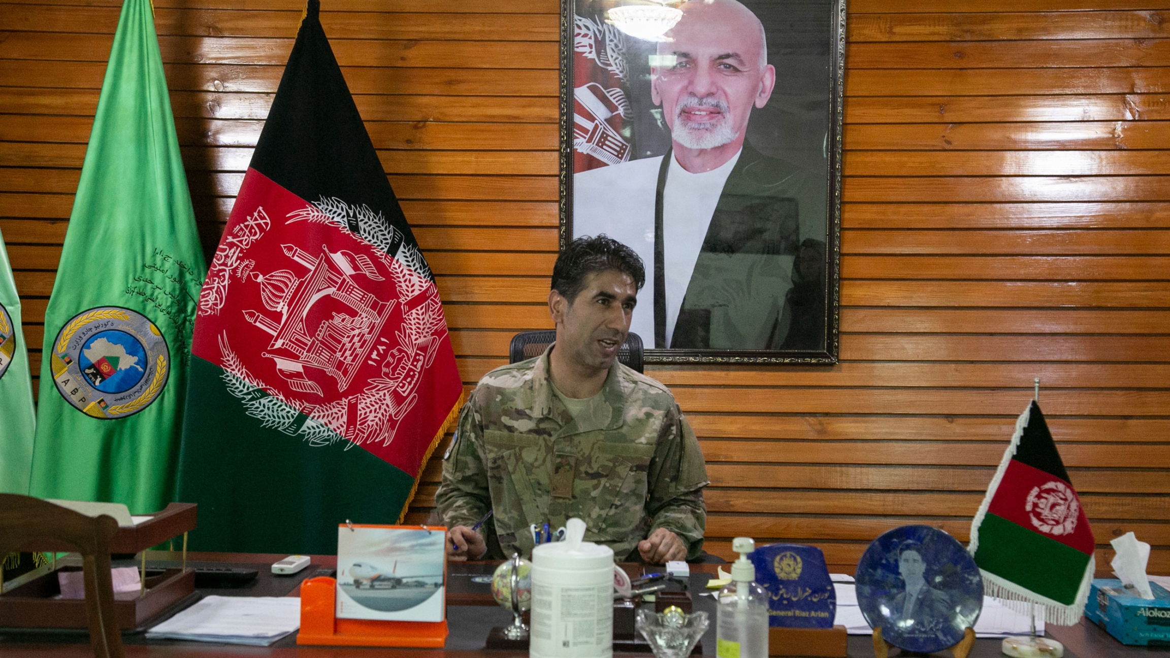 Maj. Gen. Mohammad Reyaz Arian was the top commander in charge of security at the Hamid Karzai International Airport until the Taliban takeover of Kabul. Maj. Gen. Mohammad Reyaz Arian is shown sitting at a large wooden desk and wearing military fatigues with the Afghanistan flag and a portrait photo of former President Ashraf Ghani on the wall.