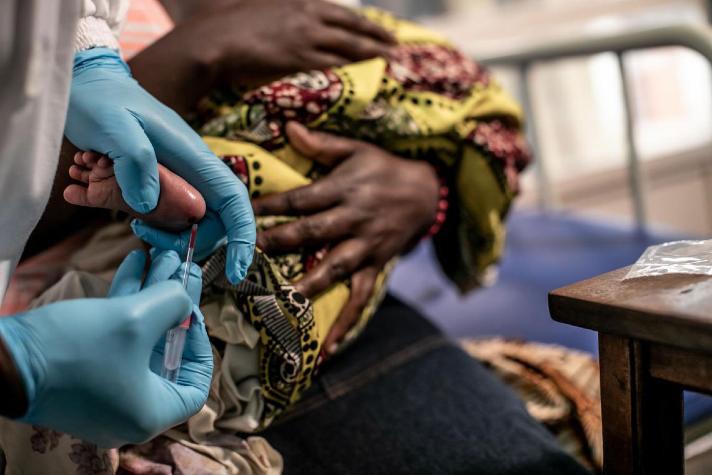A baby's blood is drawn to test for HIV. A baby's foot is pricked for a blood test by a pair of hands wearing blue gloves.