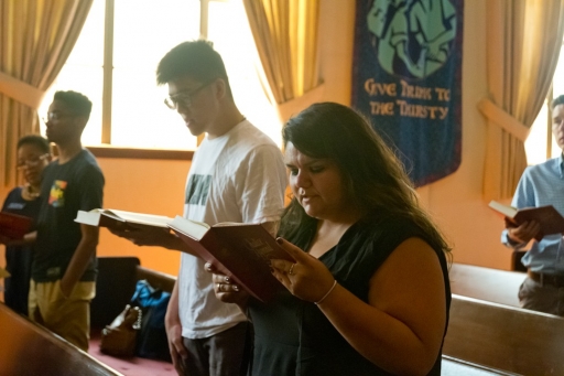 Woman in church holding book and singing, with other congregants behind her