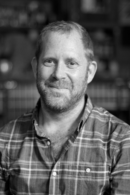 black and white portrait of man in plaid shirt smiling at camera