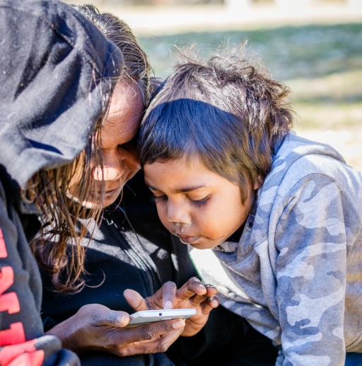 On a Sunday afternoon picnic at Telegraph Station in Alice Springs, Wyonna Palmer looks at her phone as her 6-year-old daughter, Lakayla, and her sister, Anna Maria, look on. Wyonna Palmer looking down at at her phone her daughers looking on.