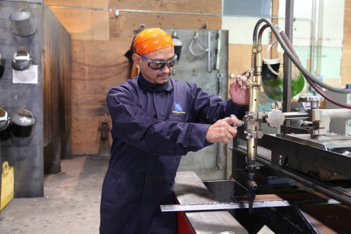 A man in welder's coveralls uses machinery in a workshop