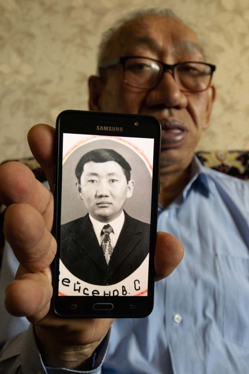 Sixty-seven-year-old Sakon Seisenuly holds a photograph of himself at the age of 22. A man wearing glasses holds up a photo of his younger self on his mobile phone.