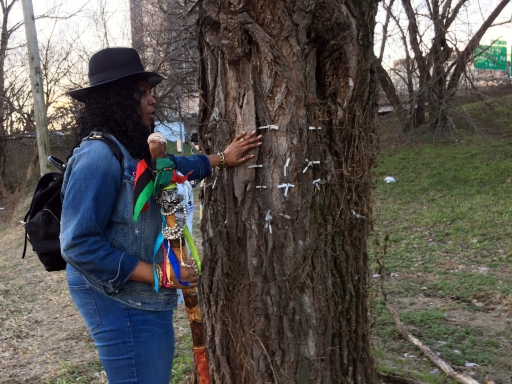 African Burial Ground A black woman in a hat stands next to a tree with tags hanging from it.