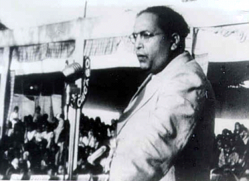 A black and white photo of a man in a suit speaking into a microphone in a crowd