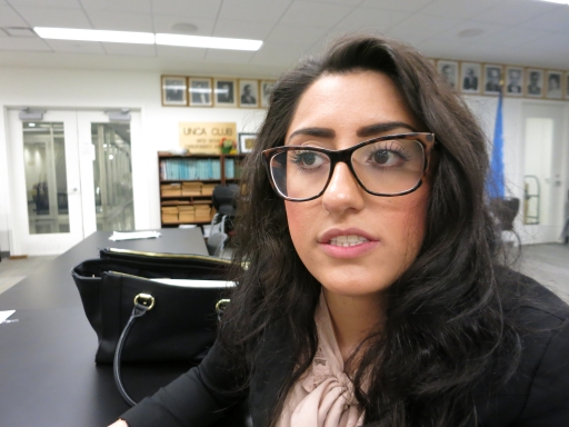 A woman in glasses sits at a desk.