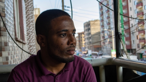 A young Kenyan Somali man looks out as he sits on deck overlooking the town. 