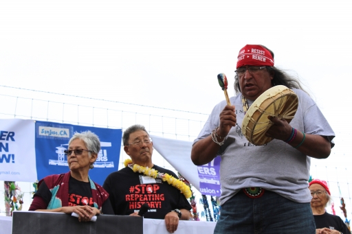 A woman and man stand behind a banner while another man plays a drum