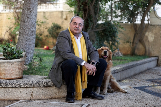 Arab politician wears yellow scarf in a suit with his dog and sits on a curb.
