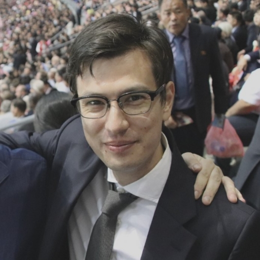 A close up of Alex Sigley in glasses and a suit with a dark tie.