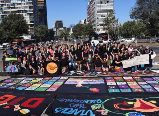 Women gathered in Santiago's Plaza Italia to hang embroidered tapestries with slogans calling for legal abortion and an end to sexual assault. Women stand near their embroidery tapestries.