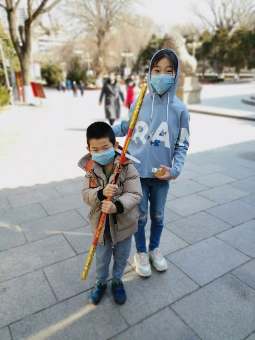Liam Hou, 6, and his sister, Francine, 10, venture outside after staying indoors for six weeks in Lanzhou, China. Two children play outside with face masks on.