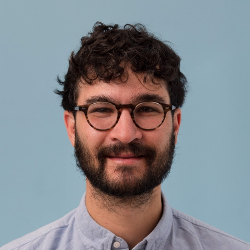 Max Rivlin-Nader A man with a beard and glasses looks at the camera.