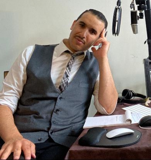 Yasser Louati is a human rights activist with Justice and Liberty for All Committee. Portrait of a man wearing a suit sitting at a table with a microphone.